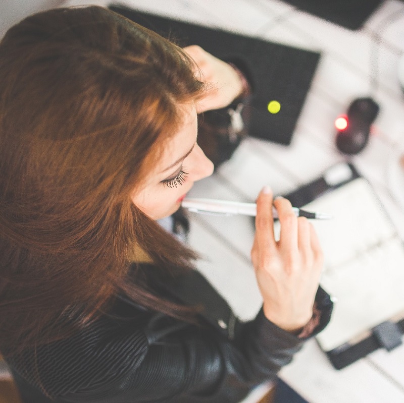 Une jeune femme réfléchit avec son carnet de note et son ordinateur